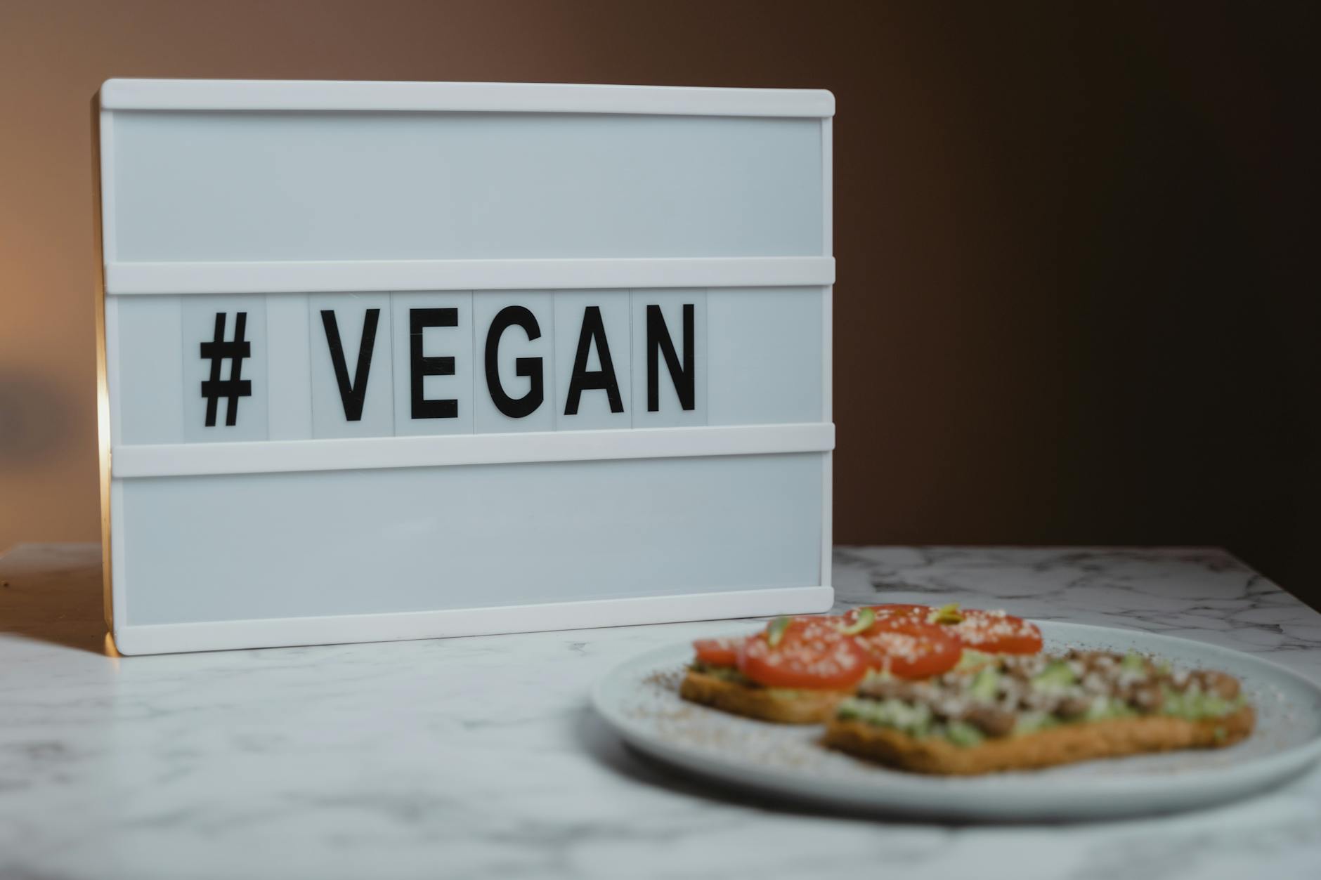 Tabliczka z napisem #VEGAN obok talerza z tostami z awokado