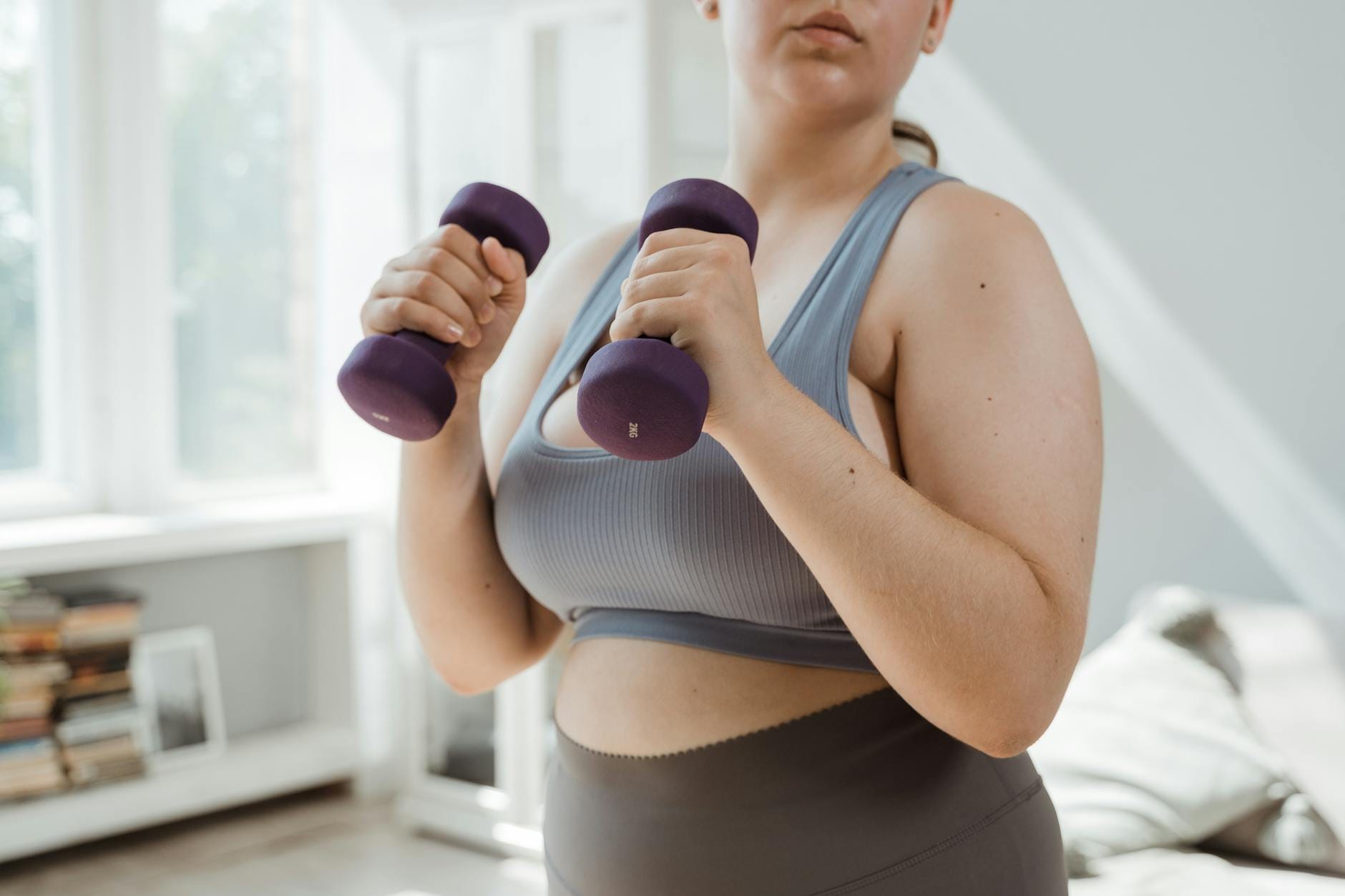 Kobieta plus size w stroju sportowym ćwiczy z hantlami w domu
