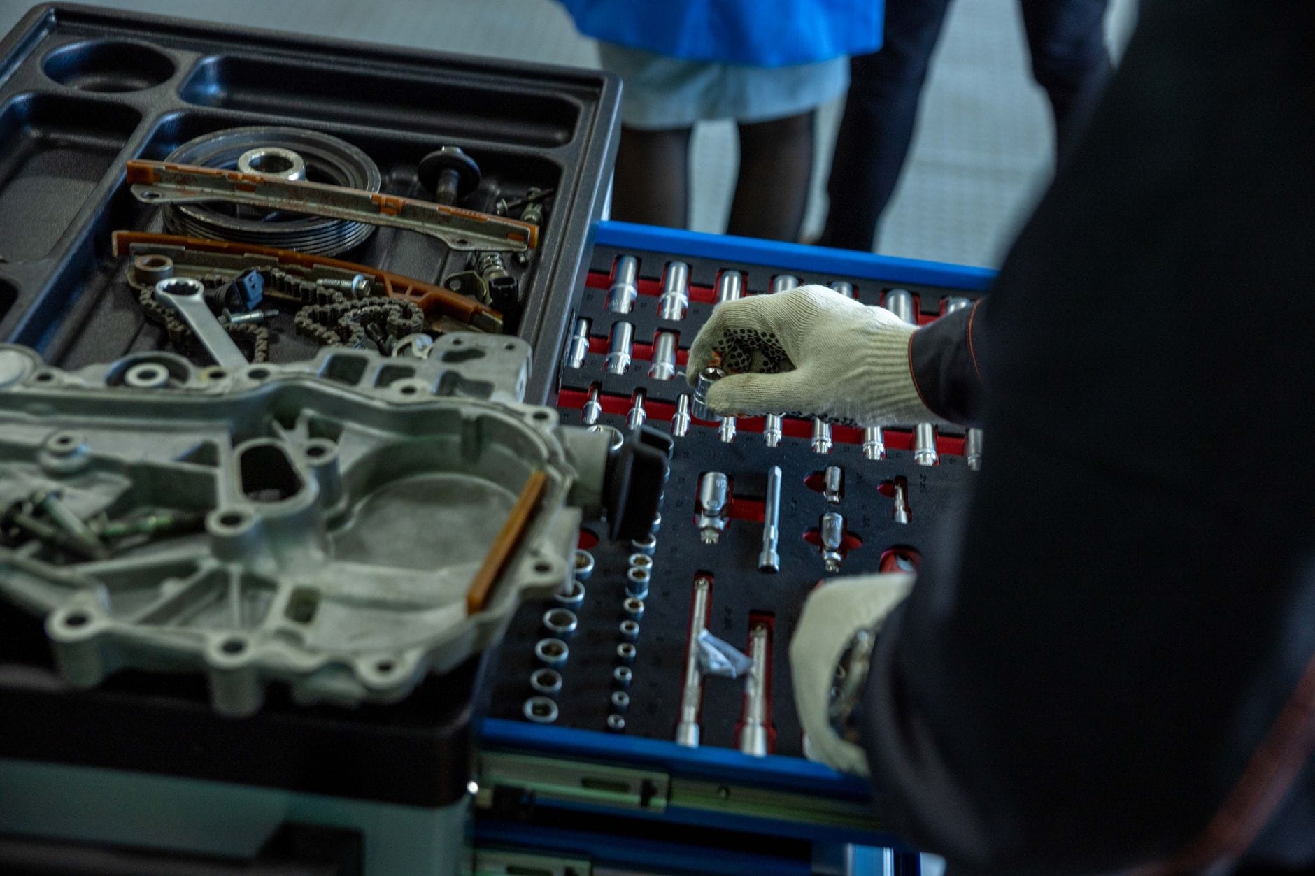 Mechanik w rękawicach układa części silnika i narzędzia w warsztacie