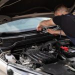 Kia 1.6 GDI a 1.6 T-GDi – który silnik wybrać w aucie używanym? Mechanik naprawiający silnik samochodowy na zewnątrz